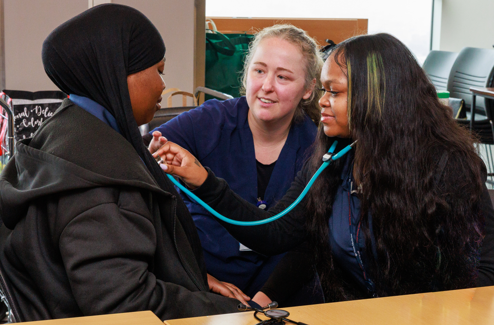 Students practice using a stethoscope as an instructor looks on.